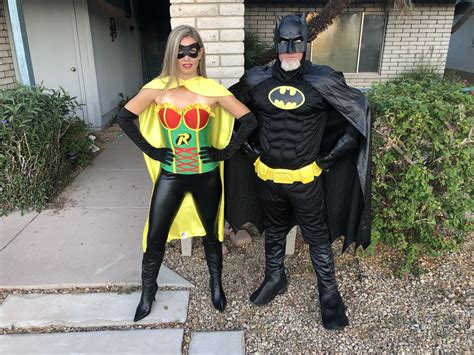 Two People Dressed Up As Batman And Robin Wayne Standing In Front Of A House With Bushes