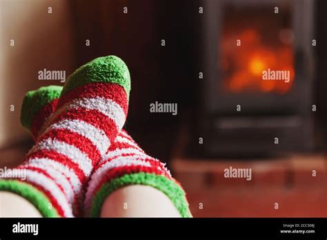 Feet legs in winter clothes wool socks at fireplace background. Woman sitting at home on winter ...