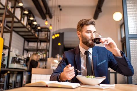 A Man Sitting At A Table With A Bowl Of Food And A Glass Of Wine