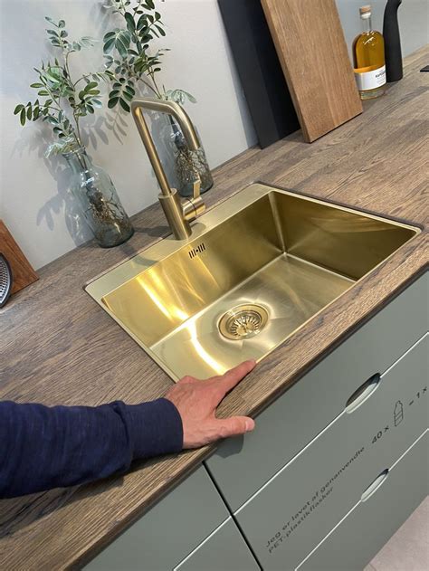 A Person Reaching For A Gold Sink In The Middle Of A Counter Top With