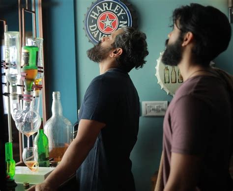 Two Men Standing In Front Of A Bar With Bottles On The Wall And One Man