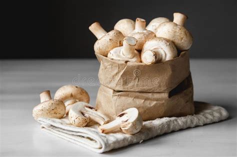 Mushrooms Champignons In Paper Bag On A White Wooden Table On A Dark