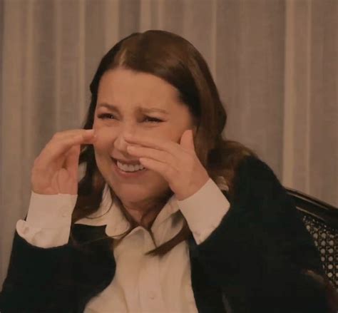 A Woman Sitting In A Chair Holding Her Hands To Her Face And Smiling At