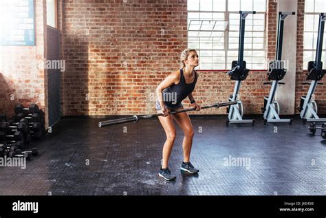 Young Woman Exercising With A Long Bar At The Gym Athlete Doing Squats