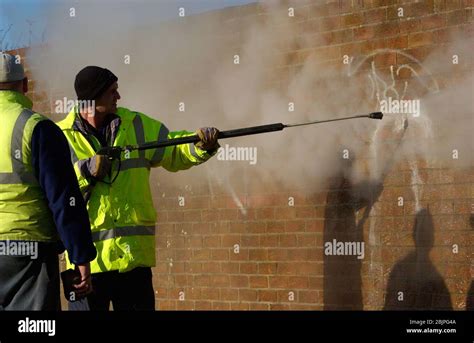 Council Worker Removing Graffiti From Wall With Steam Pressure Hose