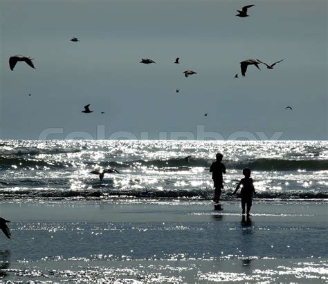 To børn leger på stranden fordi Solen Glistening på vandet Stock foto