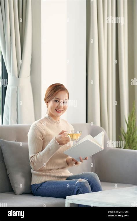 Pretty Young Woman Relaxing Reading A Book On A Comfortable Sofa At