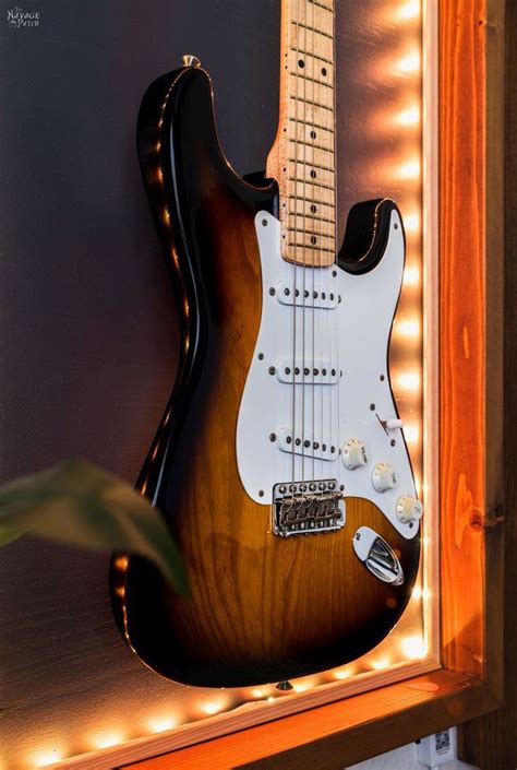 An Electric Guitar Hanging On A Wall With Lights Around It And A Plant