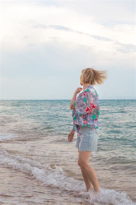 Happy Adult Blonde Woman Walking Along The Seashore On A Cloudy Summer Day Vacation At Sea