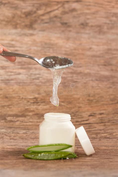 Person Placing Aloe Vera Pulp In A Plastic Container With A Metal Spoon