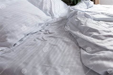 messy minimal bedroom   unmade bed white stripped satin stock