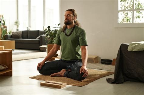 Joven sentado en posición de loto y meditando con los ojos cerrados en