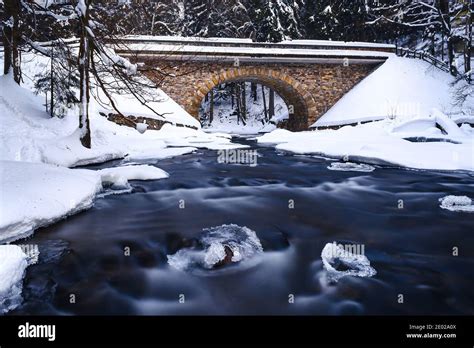 Old stone bridge over wild river in winter, surrounded by forest, snow ...