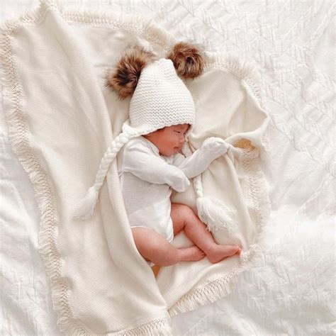 a baby wrapped in a blanket and wearing a white hat with two pompoms