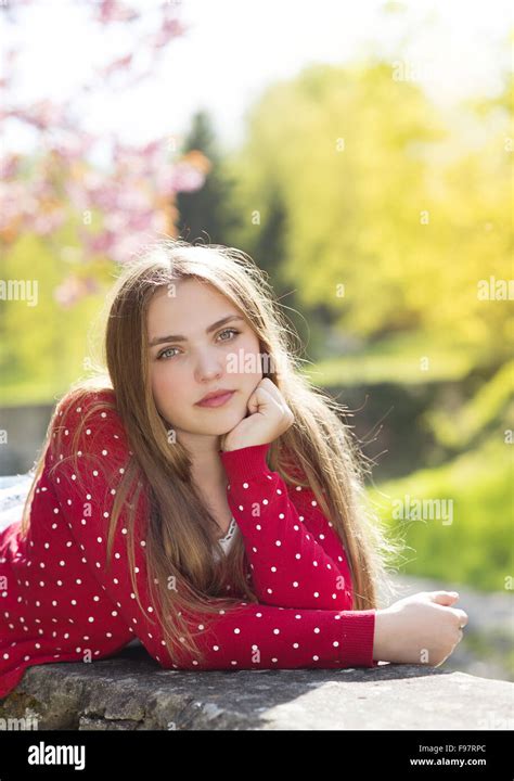 Beautiful Girl In Red Cardigan Lying On A Wall In Spring Garden With