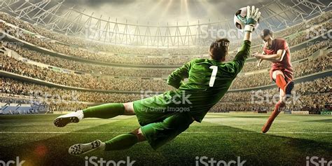 A male soccer player kicks a ball and soccer goalie jumping in motion ...