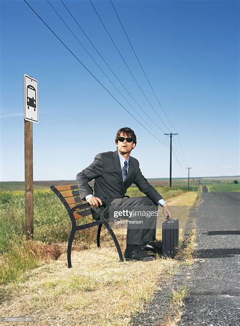 Businessman Sitting On Bench At Bus Stop With Suitcase High Res Stock