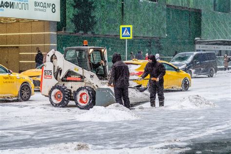 A Utility Worker And A Small Loader Excavator Remove Snow From The Road