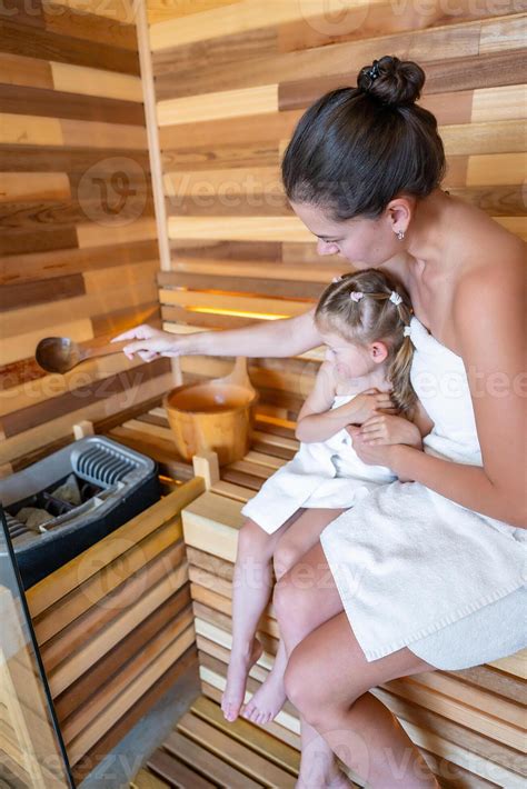 Woman Dripping Water Onto The Stove To Add Heat In The Sauna Mom And Daughter In Sauna Enjoying