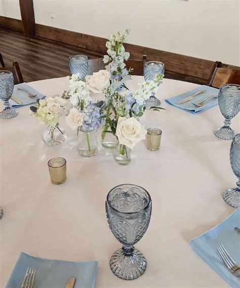 A White Table With Blue Napkins Silverware And Flowers In Vases On It