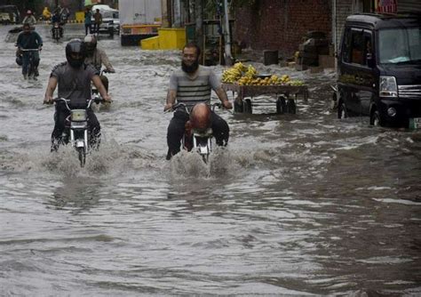 لاہور، شہری موسلا دھار بارش کے بعد سڑک پر جمع پانی میں سے گزر کر رہے ہیں۔