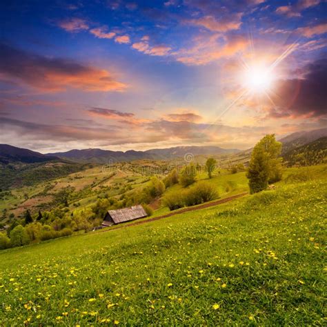 Village On Hillside Meadow With Forest In Mountain At Sunset Stock