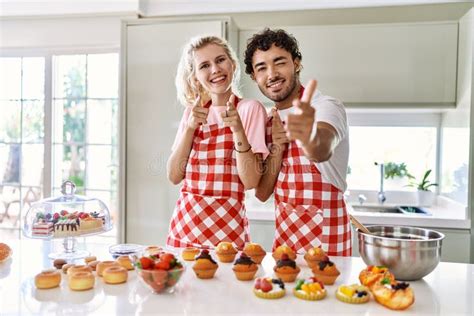 Couple Of Wife And Husband Cooking Pastries At The Kitchen Pointing Fingers To Camera With Happy