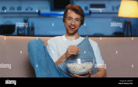 Happy Young Man Eating Popcorn While Watching Movie In Living Room