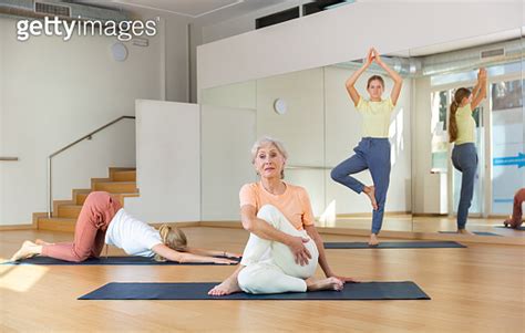 Women Doing Yoga With Group Of People In Fitness Studio Sitting In