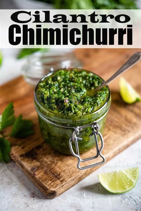 A Glass Jar Filled With Cilantro Sauce On Top Of A Wooden Cutting Board