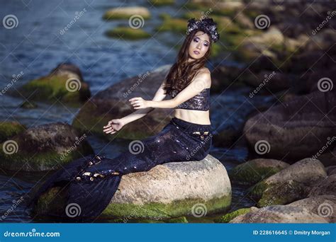 Asian Mermaid Posing Near Ocean Shore On Rocks While Wearing Seashell