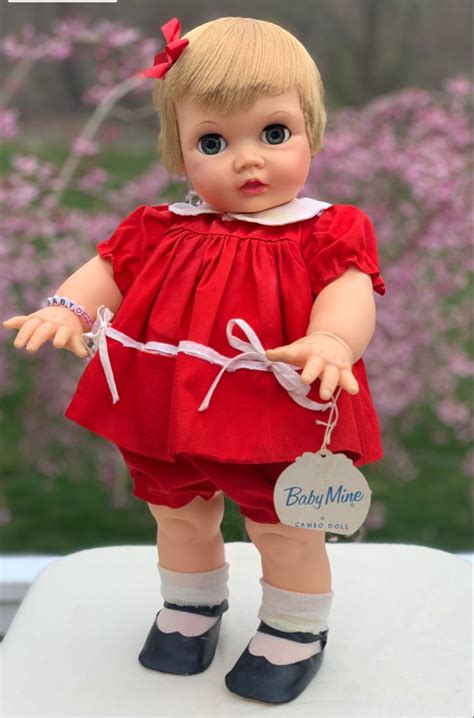 A Doll With Blonde Hair And Blue Eyes Wearing A Red Dress On A White Table