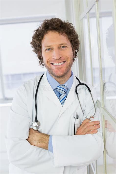 Handsome Male Doctor Standing With Arms Crossed In Hospital Stock Photo