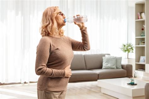 Mujer De Mediana Edad Bebiendo Agua De Una Botella De Plástico En Casa