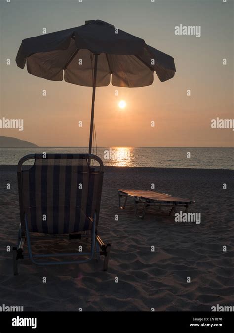 Sun bed and umbrella in Myrtos beach at sunset Stock Photo - Alamy