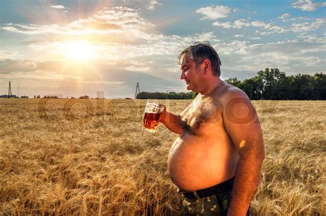 A fat man drinking beer in the field of barley | Stock image | Colourbox