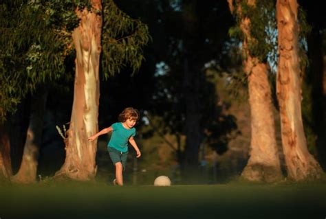 Niño emocionado niño pateando la pelota en el césped al aire libre