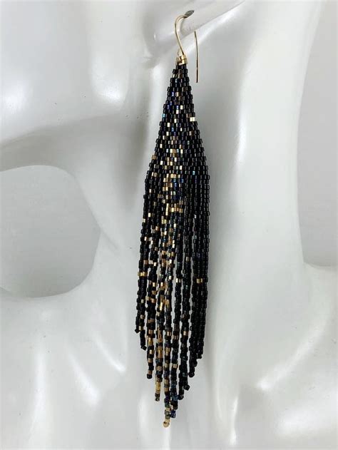 A Pair Of Black And Gold Beaded Earrings On A White Mannequin Head