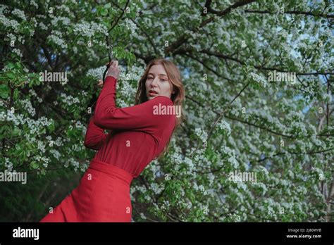 A Blonde Girl In Red Hides In Flowering Trees Stock Photo Alamy