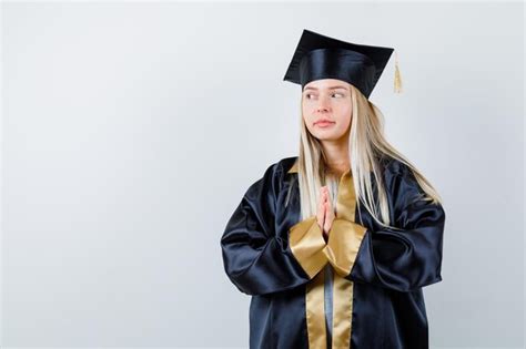 금발 소녀 졸업 가운과 모자에 제스처를기도하고 심각한 찾고 손을 Clasping 무료 사진