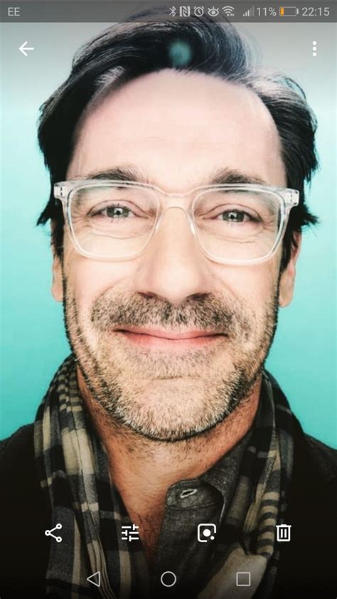 A Man With Glasses And A Scarf On His Neck Is Looking At The Camera While Smiling