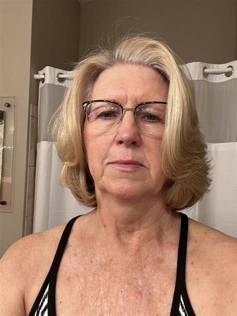 An Older Woman With Glasses Is Looking At The Camera In Front Of A