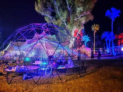 An Outdoor Tent Lit Up At Night With Palm Trees In The Background And