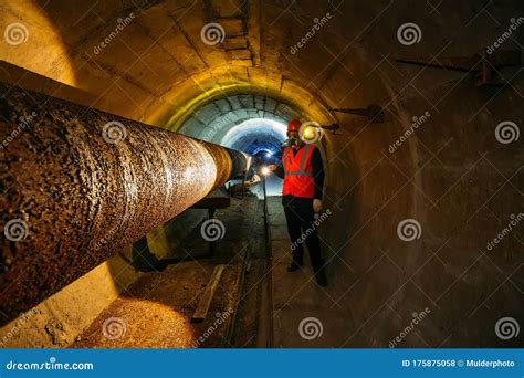 Tunnel Worker Examines Pipeline In Underground Tunnel Stock Photo