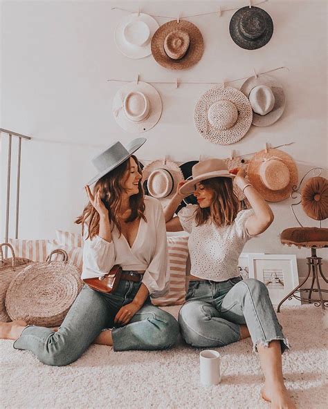 Two Women Sitting On The Floor In Front Of Hats Hanging From The Wall