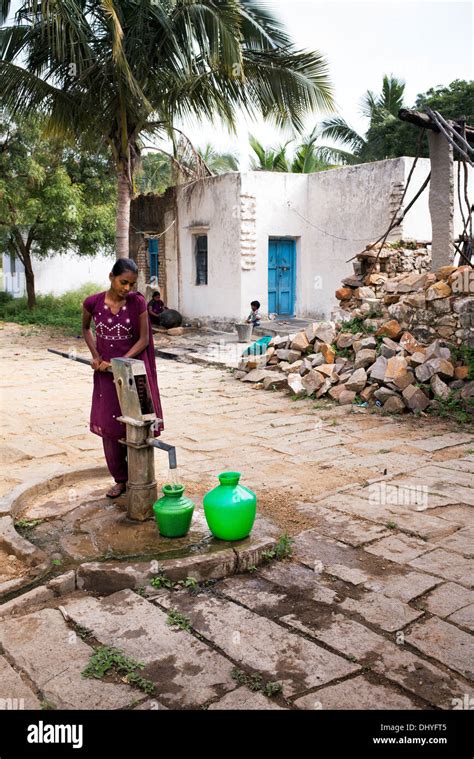 Indian Teenage Girl Pumping Water From A Hand Pump Into A Pot In A