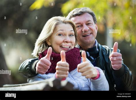 Loving Mature Couple Cuddling In Park And Showing Thumbs Up Stock Photo