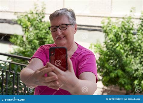 Une Femme Plus âgée Est Assise Sur Sa Terrasse à La Maison Elle Tient Un Smartphone Rouge Et