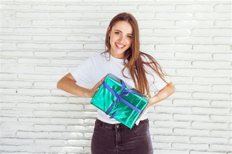 Mujer Joven Feliz Que Sostiene La Caja De Regalo Delante De La Pared De