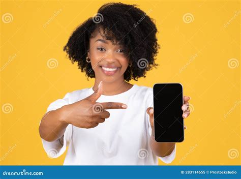 Glad Millennial Black Lady In Casual Pointing Finger At Phone With